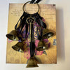 Decorative metal wind chimes hanging from a black leather strap on aged paper.