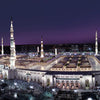 Night view of the Masjid an Nabawi mosque with minarets illuminated against a dark sky.