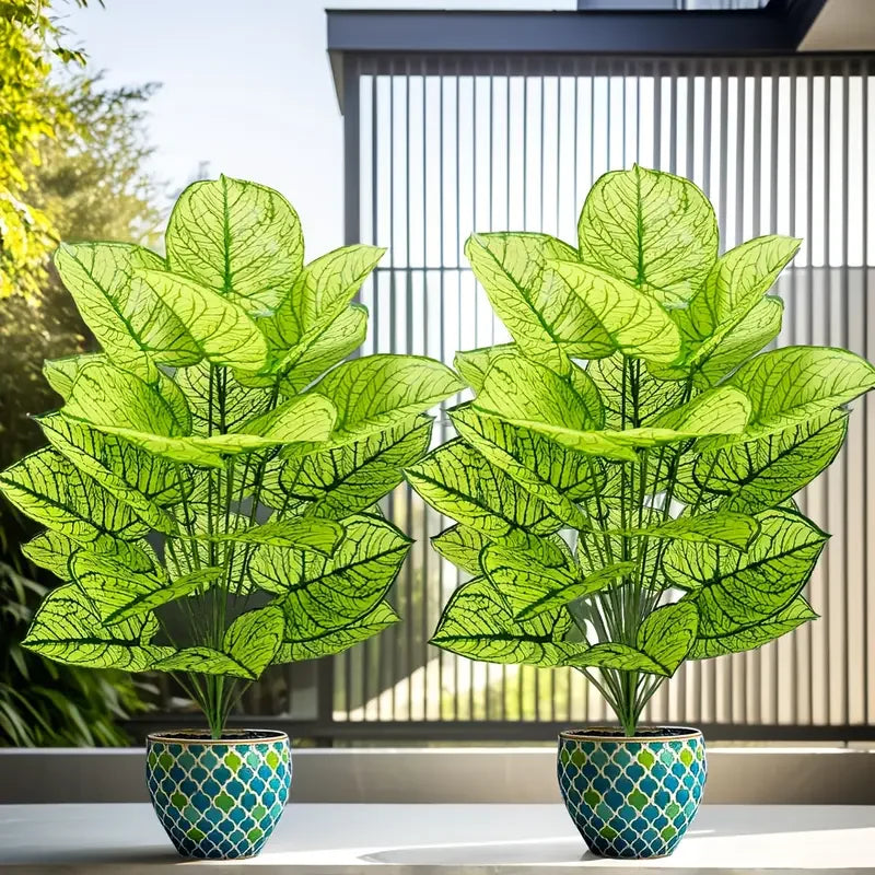 A set of two realistic artificial floor plants with large green leaves displayed on a white surface.