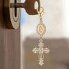 Gold pearl rhinestone cross keychain charm hanging from a door hook.