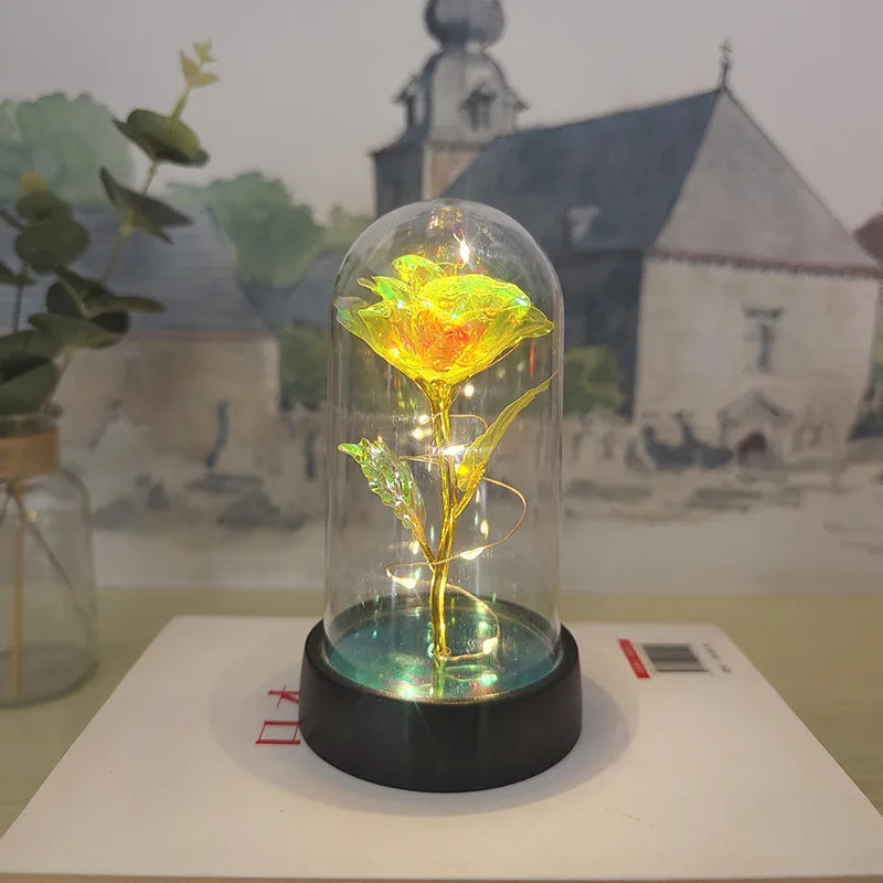 Rose de verre éternelle avec une lumière LED affichée dans une coupole en verre, sur fond de scène de village.