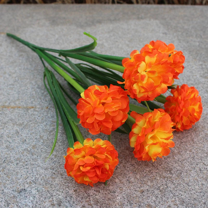 Un bouquet de fleurs artificielles ressemblant à des soucis oranges et jaunes avec des tiges vertes sur une surface grise.
