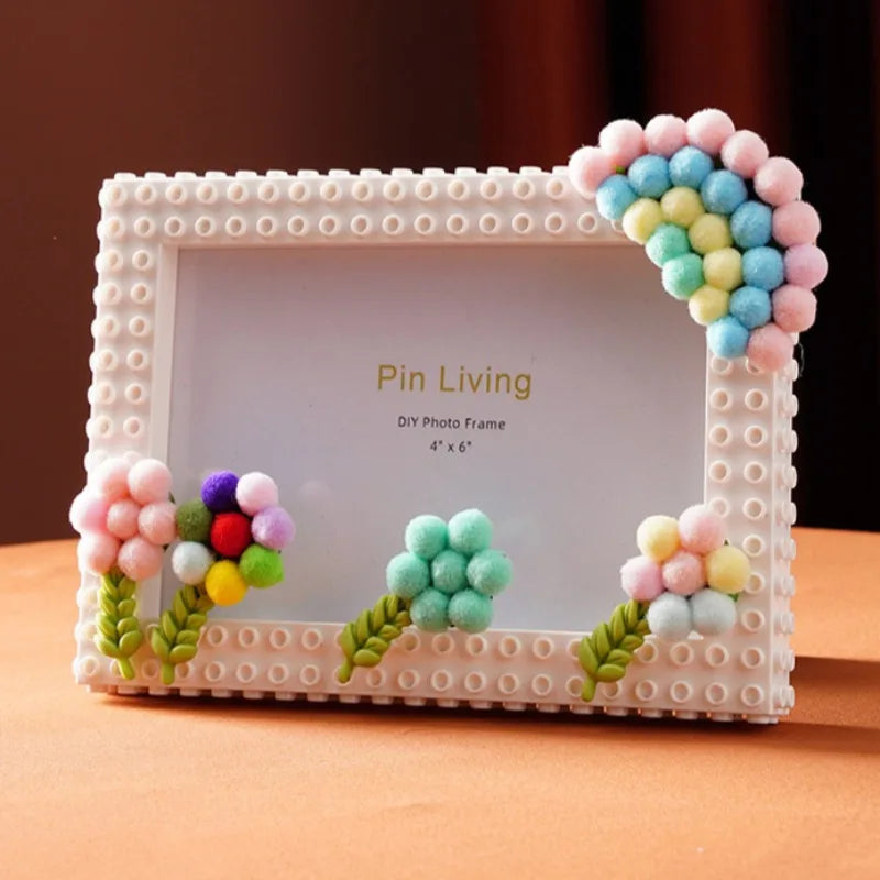 A white photo frame decorated with pink and blue fabric flowers and green leaves, featuring a 'Pin Living' theme.