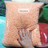 A hand is holding a clear bag filled with orange pastel foam beads for crafting and decoration.
