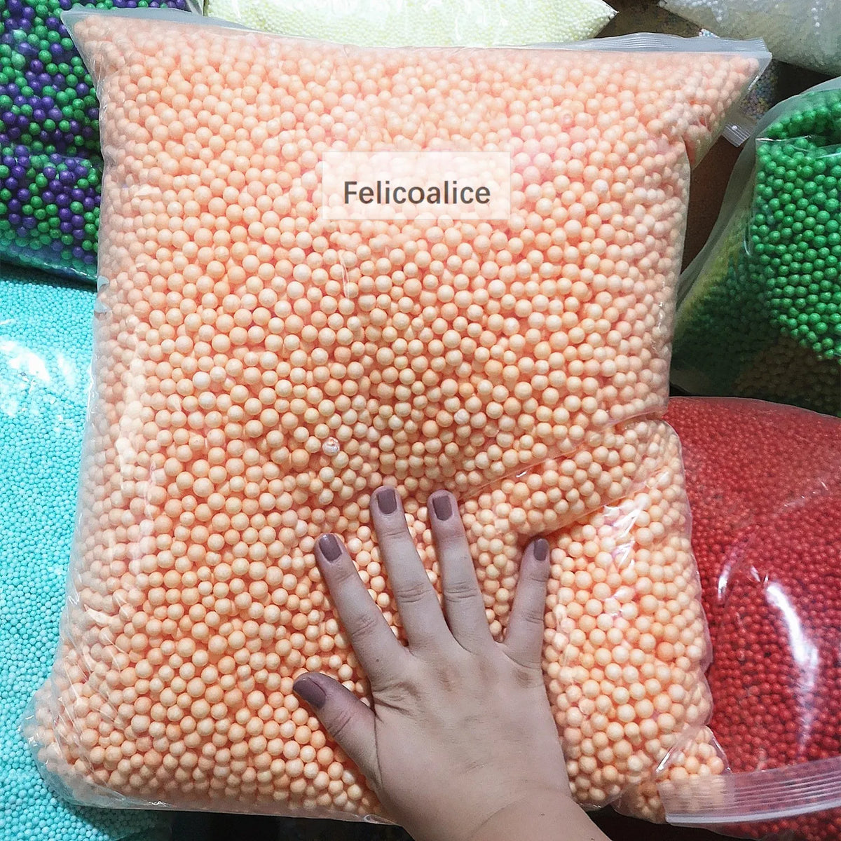 A hand is holding a clear bag filled with orange pastel foam beads for crafting and decoration.