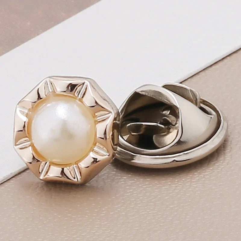 A close-up of a gold-toned pearl and rhinestone no-sew brooch button on a white background.