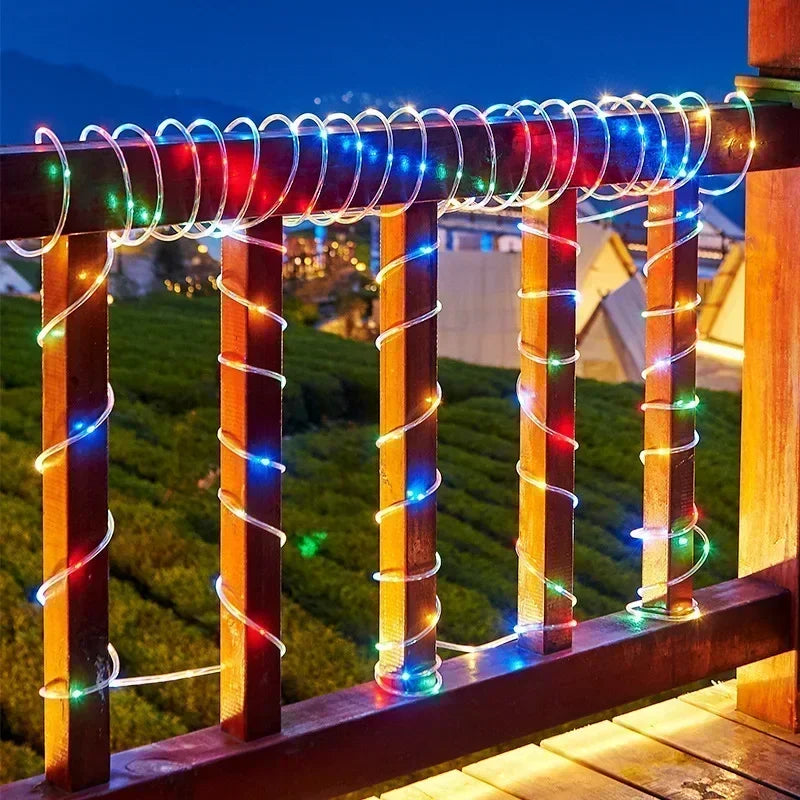 A wooden railing decorated with colorful LED rope lights illuminating a scenic outdoor view at night.