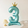 A teal foil balloon shaped like the number three with a gold crown on top.