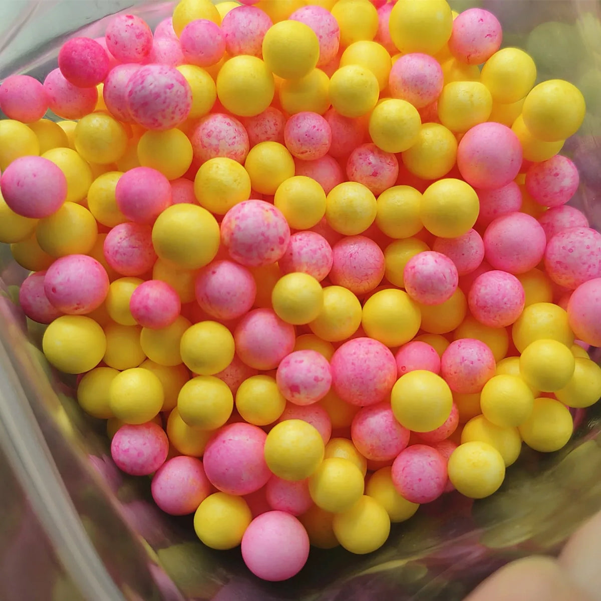 A close-up view of numerous pastel foam beads in shades of pink and yellow filling a clear container.