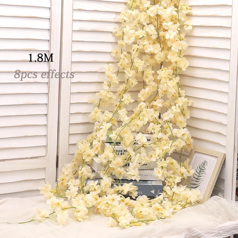 A long garland of artificial pale yellow sakura flowers draped against a white wooden background.