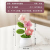 A pink and green hand-woven crochet flower potted plant displayed on a white surface.
