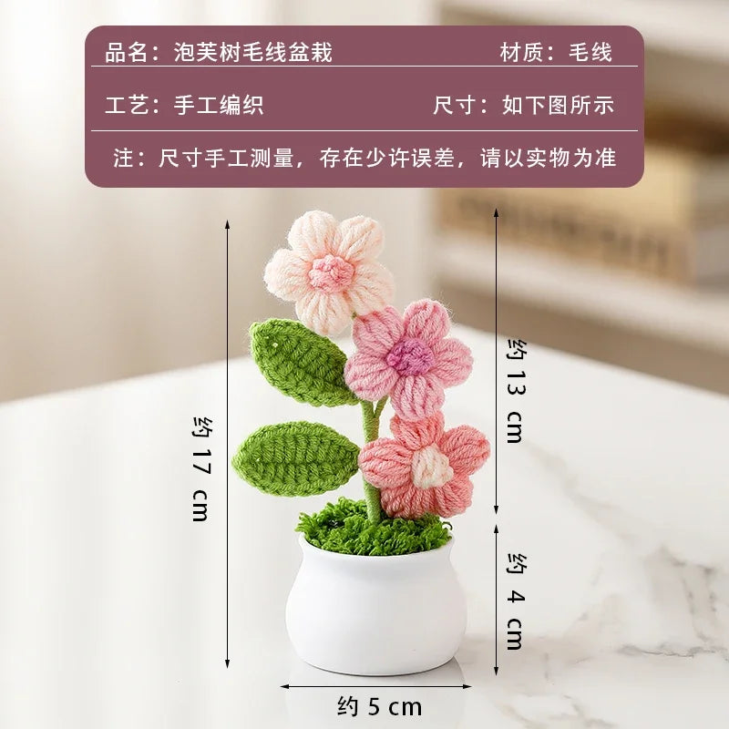 A pink and green hand-woven crochet flower potted plant displayed on a white surface.