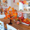 Une décoration lumineuse d'un arbre de bouleaux noirs artificiel avec des feuilles d'automne orange et rouge sur une table en