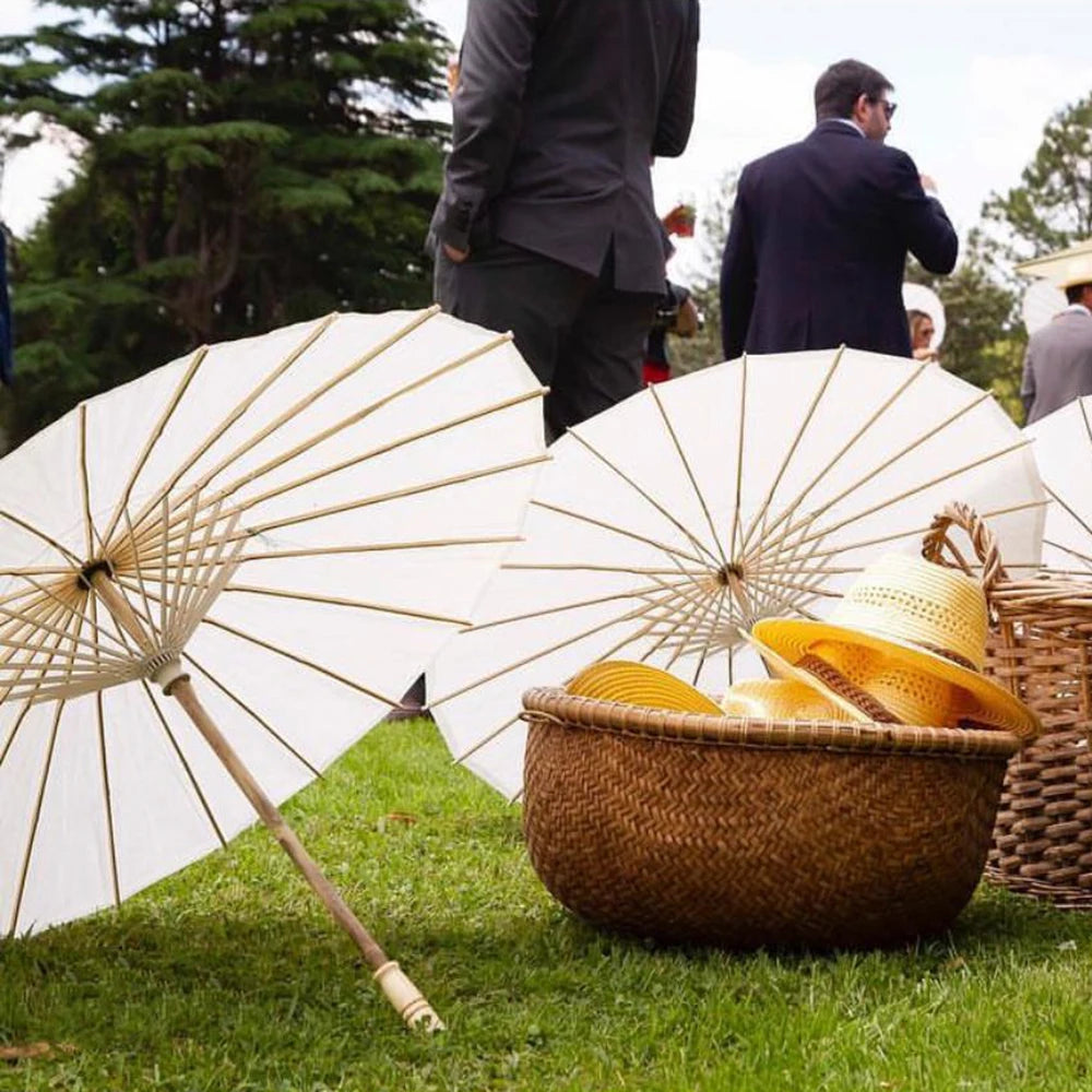 Several white decorative paper parasols are displayed next to a woven basket on green grass.