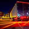 A large truck with bright LED side marker lights illuminating the road at night.