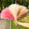 A hand holds a bouquet of pink, cream, and tan artificial pampas grass reeds for home and event decor.