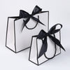 A set of five elegant black and white gift bags tied with black ribbon bows.
