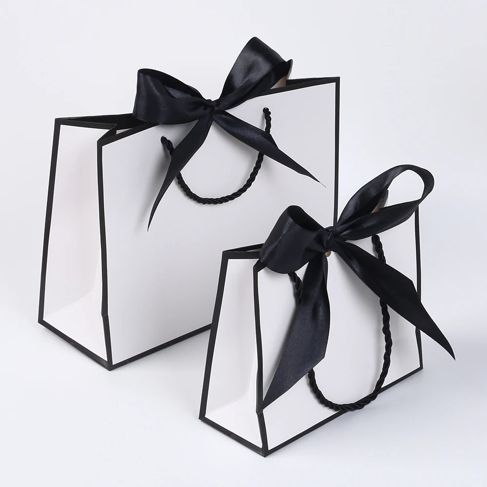 A set of five elegant black and white gift bags tied with black ribbon bows.