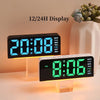 A black digital alarm clock displaying 20:08 on a wooden stand, with an accompanying white vase and greenery.