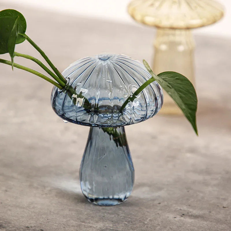 A clear glass vase shaped like a mushroom with translucent blue and white jelly colors sits on a gray surface.