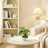 A green potted plant sits on a white round table next to a light-colored sofa and bookshelf.