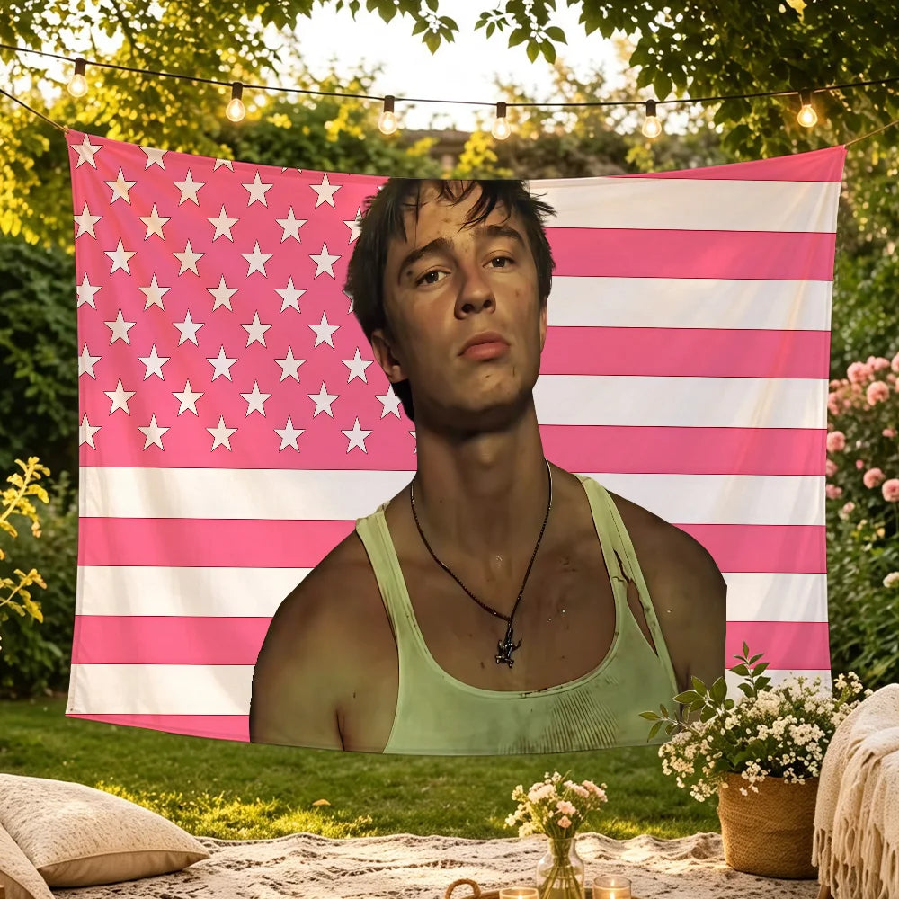 A young man wearing a pink and white American flag tapestry in an outdoor setting.