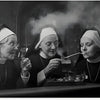 Trois religieuses en habits noirs fument des pipes tout en regardant un verre de boisson.