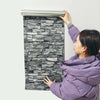 Une femme applique des autocollants waterproof 3D sur un mur blanc, créant une texture de pierre.