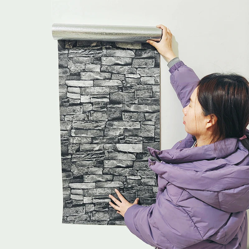 Une femme applique des autocollants waterproof 3D sur un mur blanc, créant une texture de pierre.