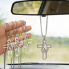 Stainless steel praying hands cross pendant hanging from a chain displayed in front of a car mirror.