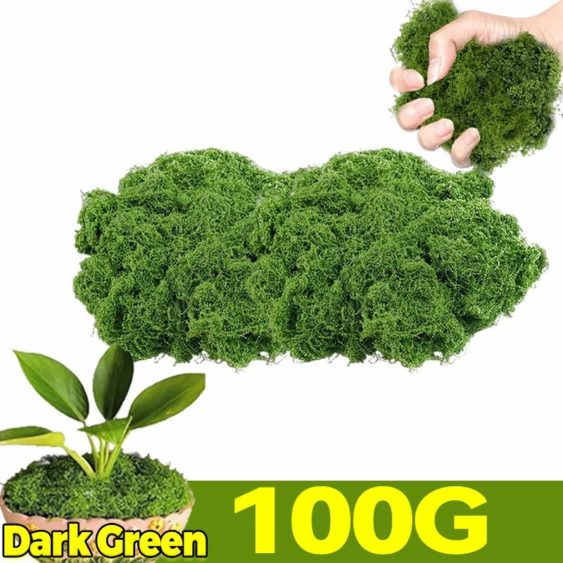 A hand is holding a clump of dark green artificial moss, with a larger mass of the same moss visible below.