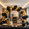 A black and gold balloon garland arch decoration for an event, set up on a table with place settings.