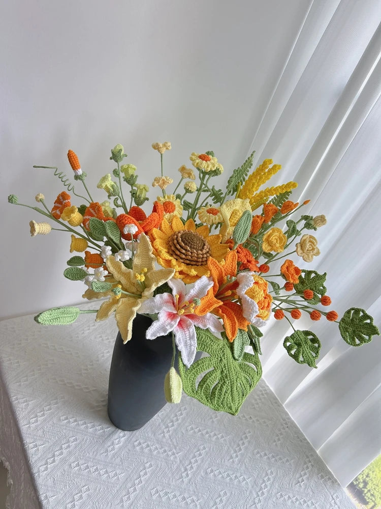 Ramo de flores de ganchillo artesanal con flores naranjas, amarillas y blancas y follaje verde en un jarrón negro.