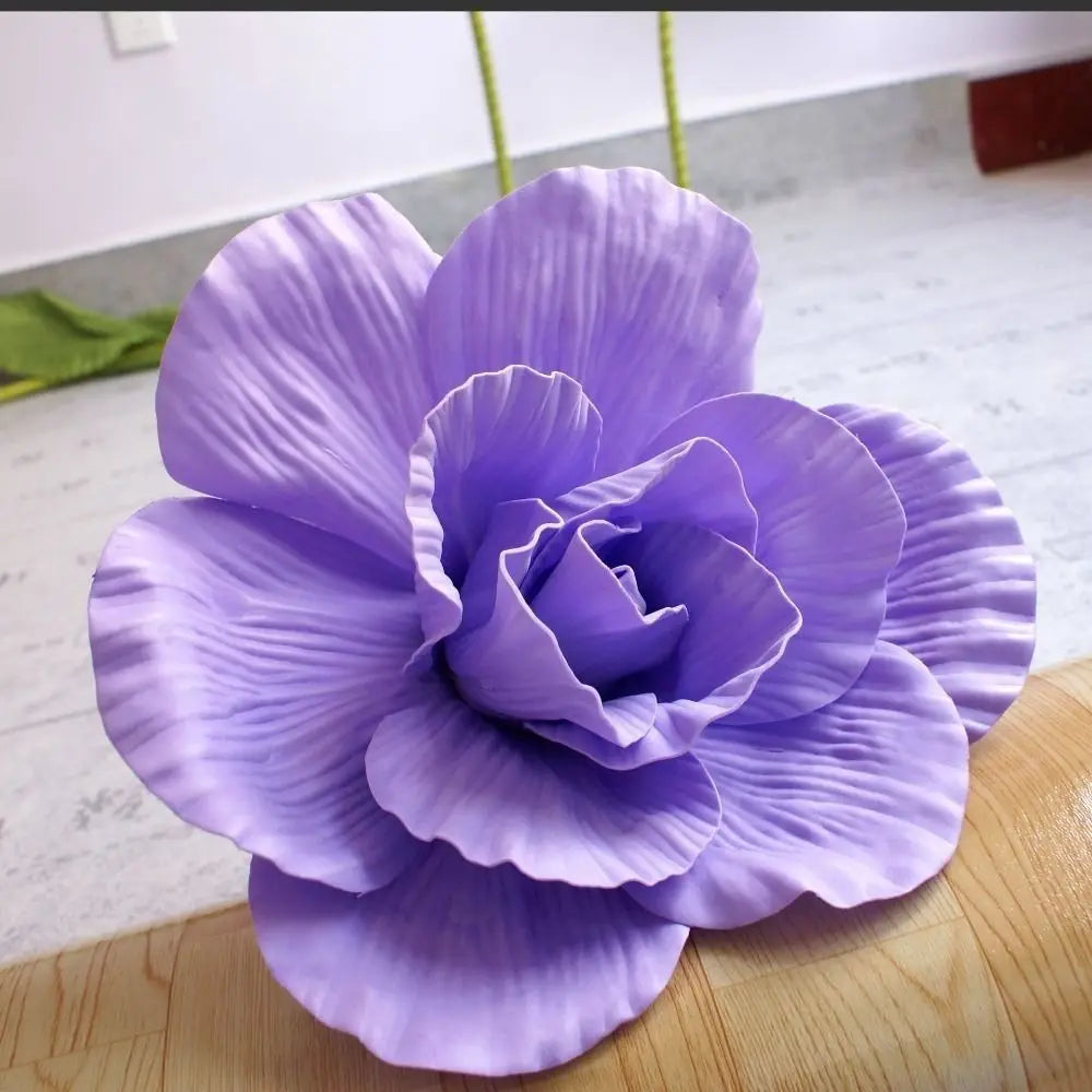A vibrant purple silk foam rose flower in full bloom displayed on a wooden surface.