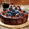 A round chocolate cake topped with fresh blueberries and blackberries, served on a wooden board.