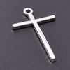 A silver cross charm with a loop, displayed against a dark gray background.