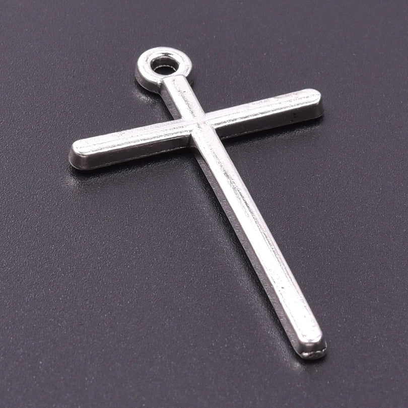 A silver cross charm with a loop, displayed against a dark gray background.