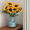 A bouquet of bright yellow and dark center sunflowers in a modern blue ceramic tabletop vase.