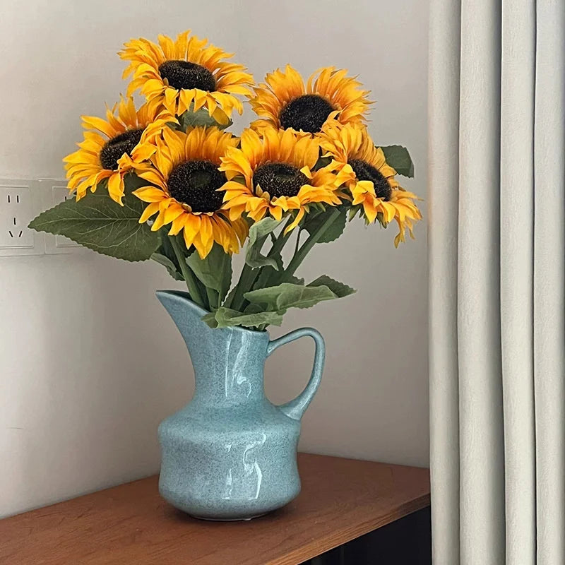 A bouquet of bright yellow and dark center sunflowers in a modern blue ceramic tabletop vase.