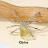 Handcrafted crystal spider figurine with a yellow citrine body resting on a wooden surface.