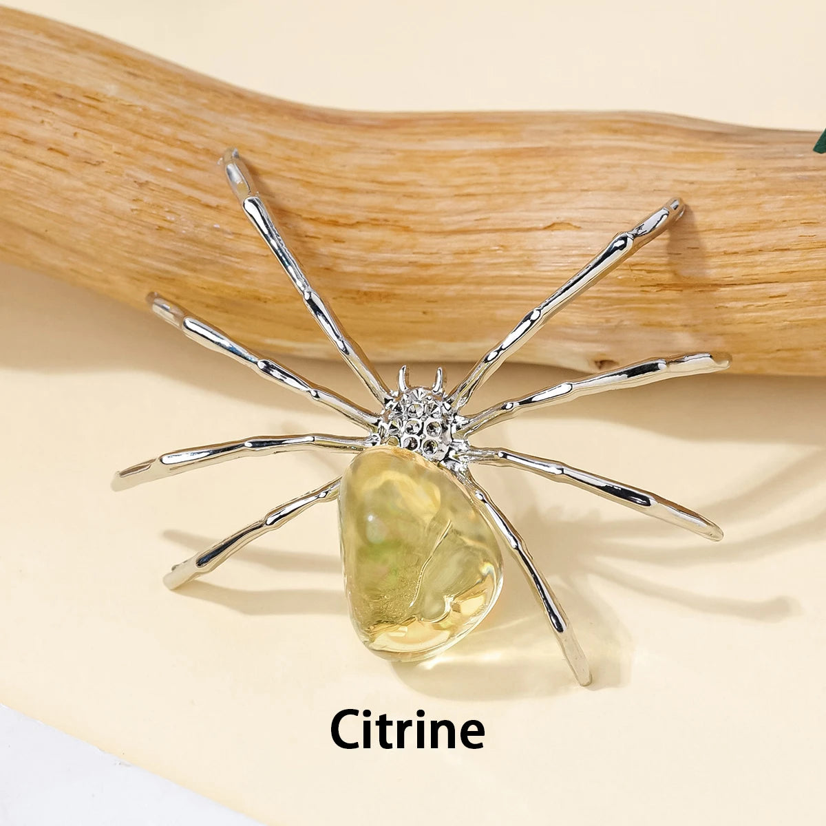Handcrafted crystal spider figurine with a yellow citrine body resting on a wooden surface.