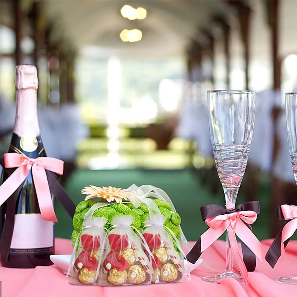 Elegant white and gold drawstring organza bags for gifts displayed on a pink table.