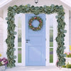A light blue door framed by a lush green eucalyptus leaf garland and floral wreath for home decor