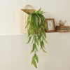 Kunststoff-Eukalyptus-Pinienranken-Wanddekoration mit grünen Blättern in einem geflochtenen Korb neben einem gerahmten Bild