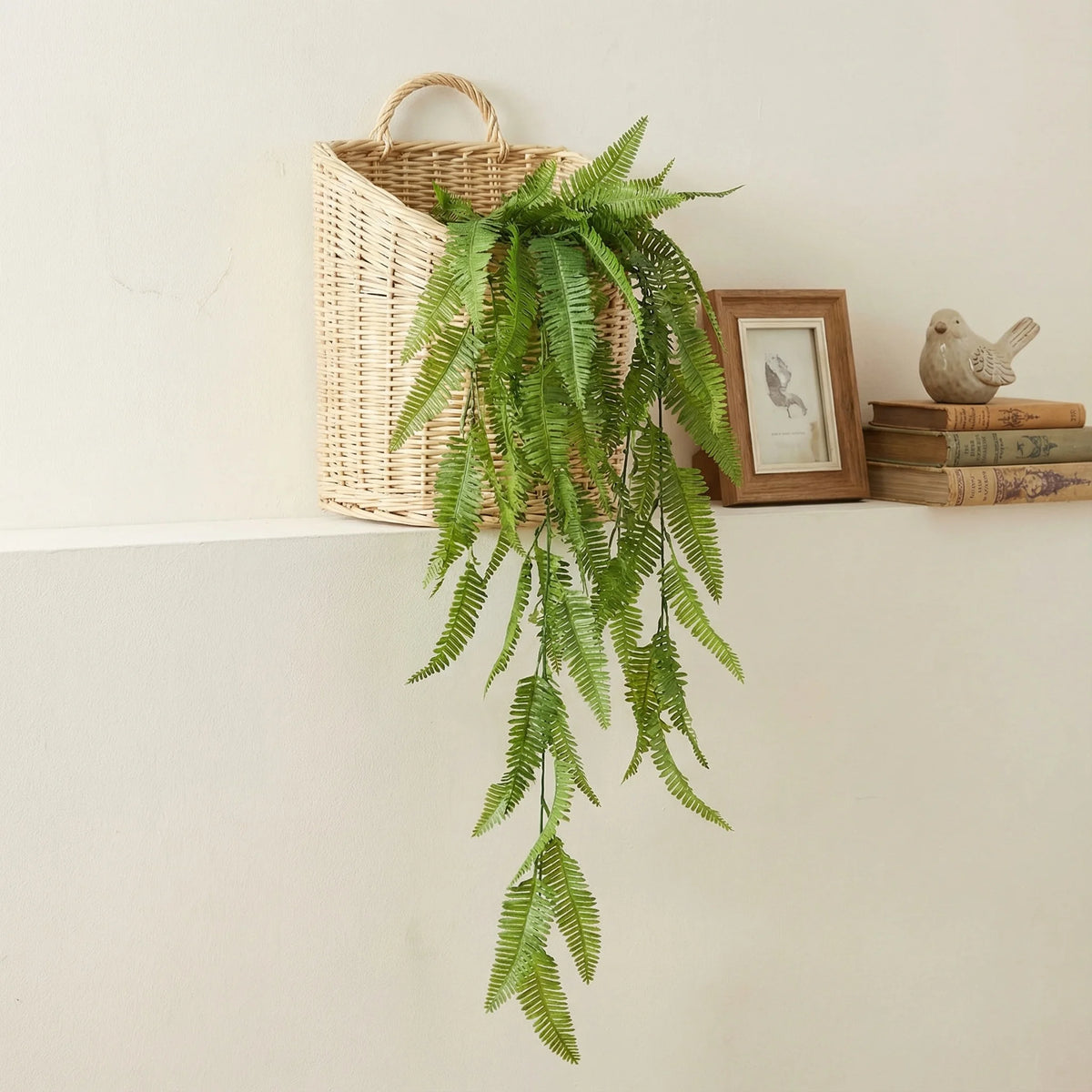Kunststoff-Eukalyptus-Pinienranken-Wanddekoration mit grünen Blättern in einem geflochtenen Korb neben einem gerahmten Bild