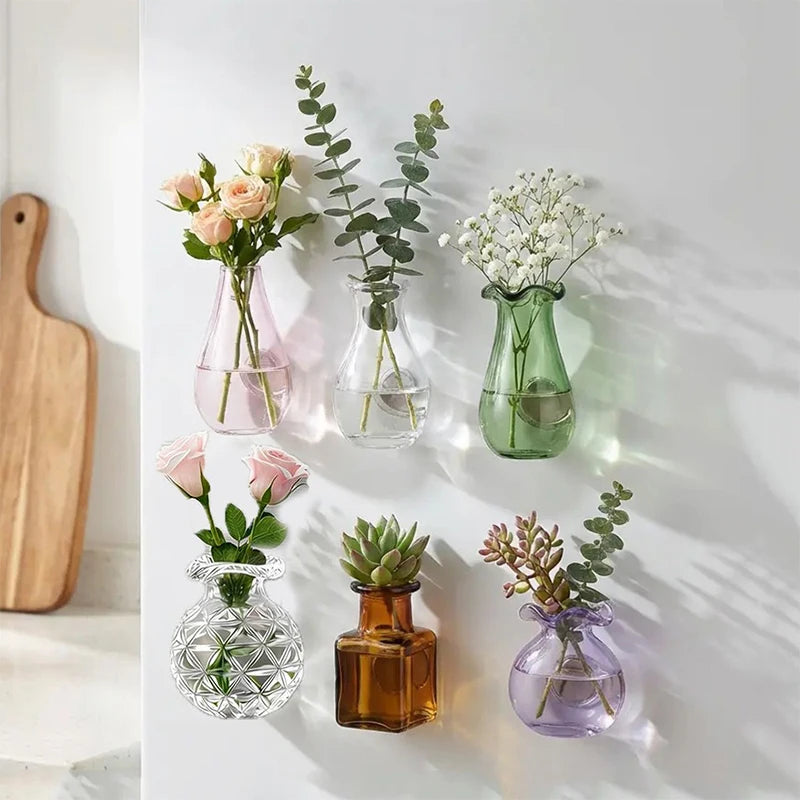 Eine Sammlung magnetischer Kühlschrankmagneten mit getrockneten Blumen und Grünzeug in Glasflaschen.