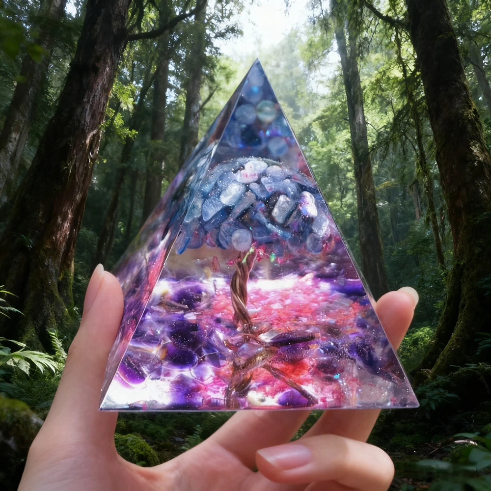 Hand holding a clear resin pyramid with natural obsidian and copper coil inside, set in a lush forest environment.