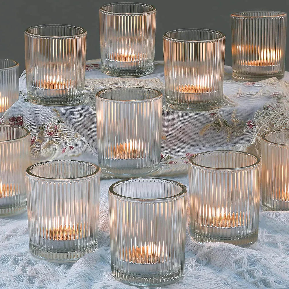 A collection of clear glass votive candle holders with vertical stripes arranged on a white lace fabric.