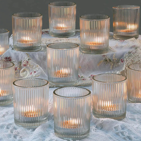 A collection of clear glass votive candle holders with vertical stripes arranged on a white lace fabric.