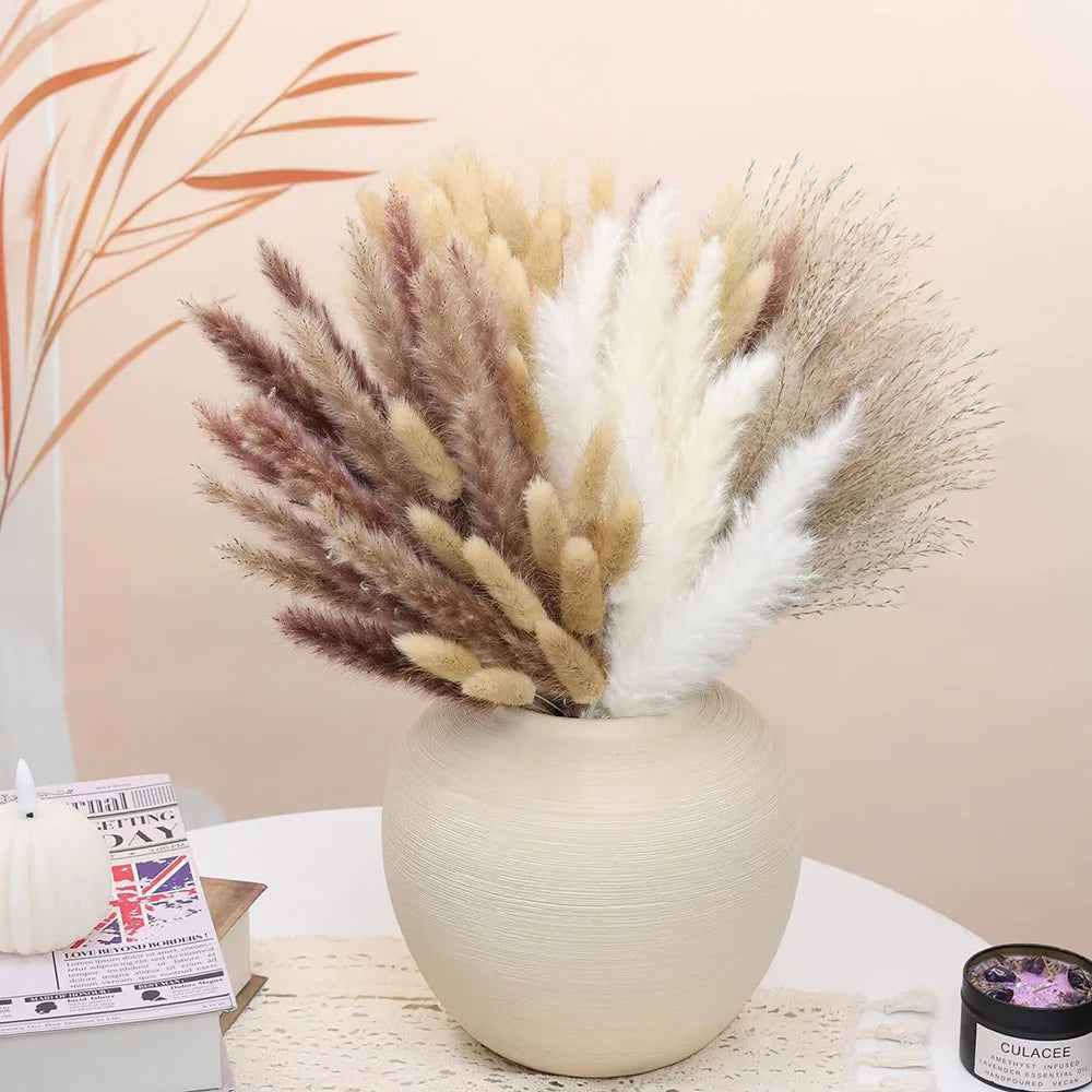 باقة زهور مجففة من نبات القش (Pampas grass) بألوان البيج والبني والكريمي في مزهرية سيراميك فاتحة.